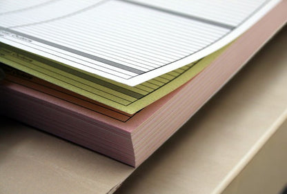 Stack of perforated A5 N.C.R. pads in a fanned out arrangement, showing the top page with structured lines and text boxes.