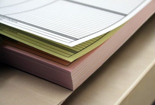 Stack of perforated A5 N.C.R. pads in a fanned out arrangement, showing the top page with structured lines and text boxes.